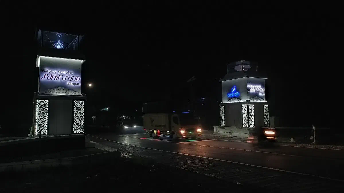 Two illuminated city gate towers with lit welcome signage beside a road at night