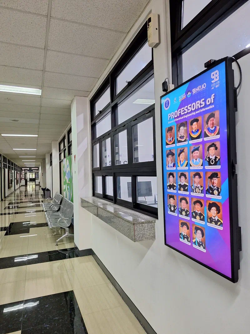 Wall-mounted screen in a STEI corridor showing the school's professors