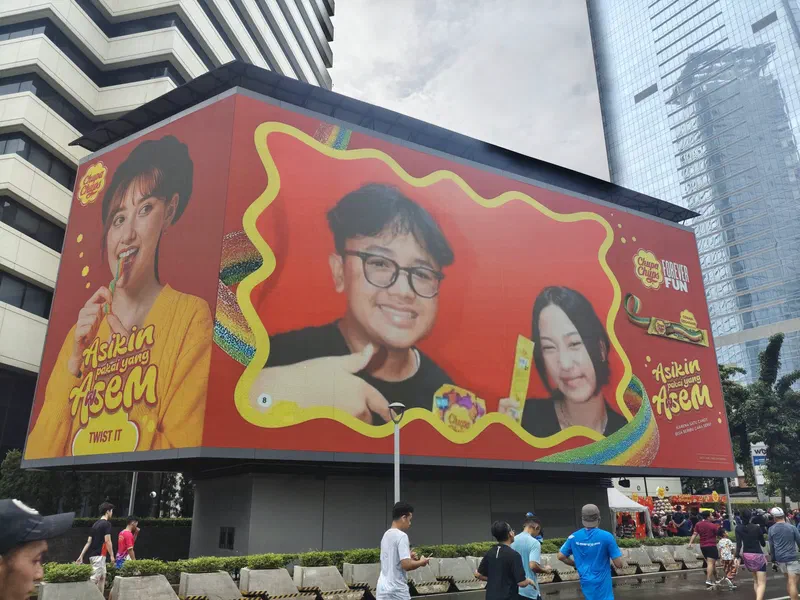 Videotron LED showing two visitors' photobooth photo in the Chupa Chups campaign frame, above runners on the street
